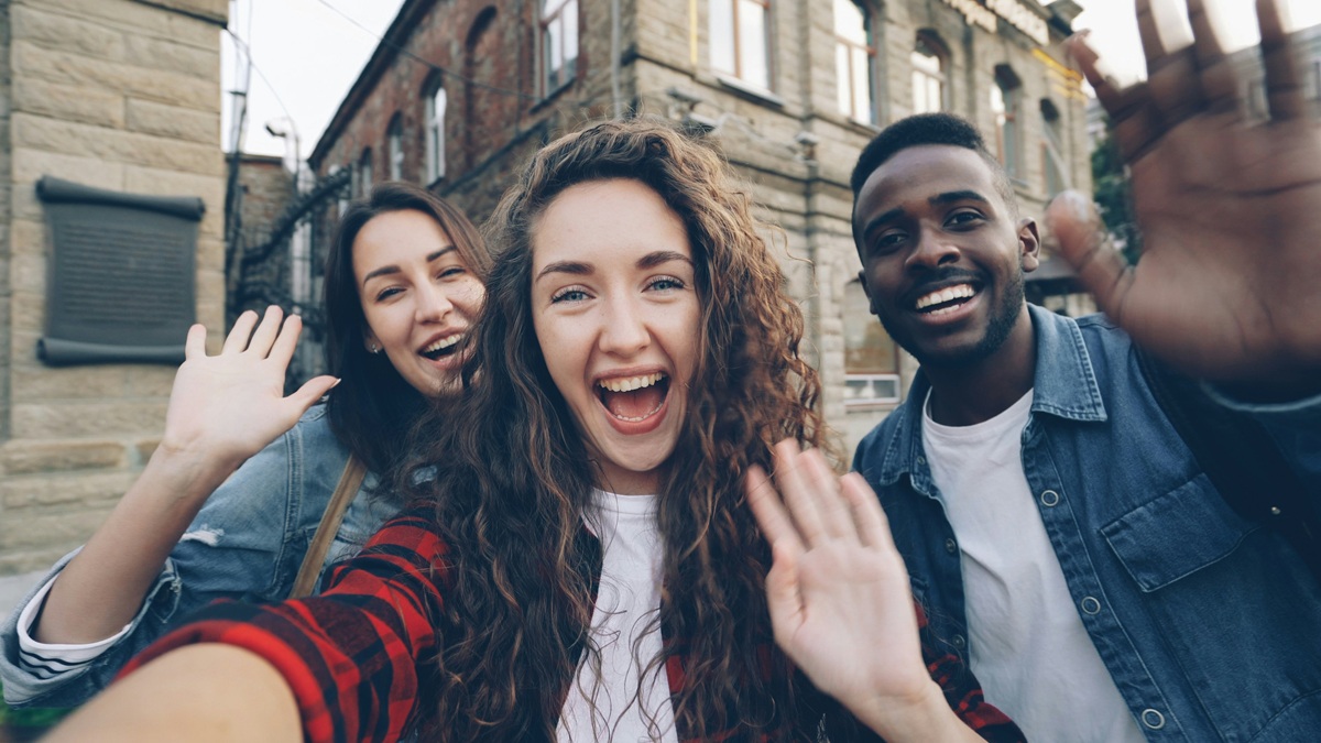 A diverse group of three young people smiling and waving warmly, representing the welcoming community at BrightSteps Foundation.