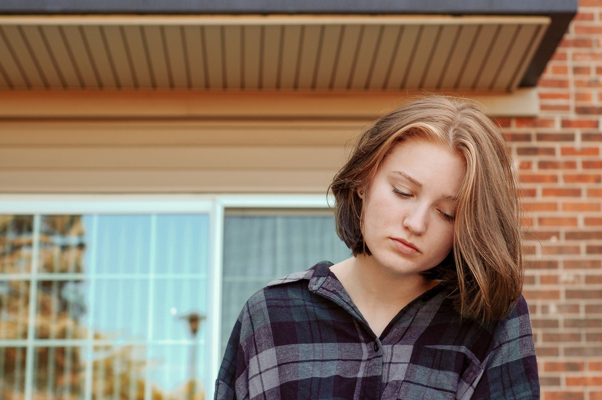 A young person standing outdoors, looking down in a quiet, reflective moment.