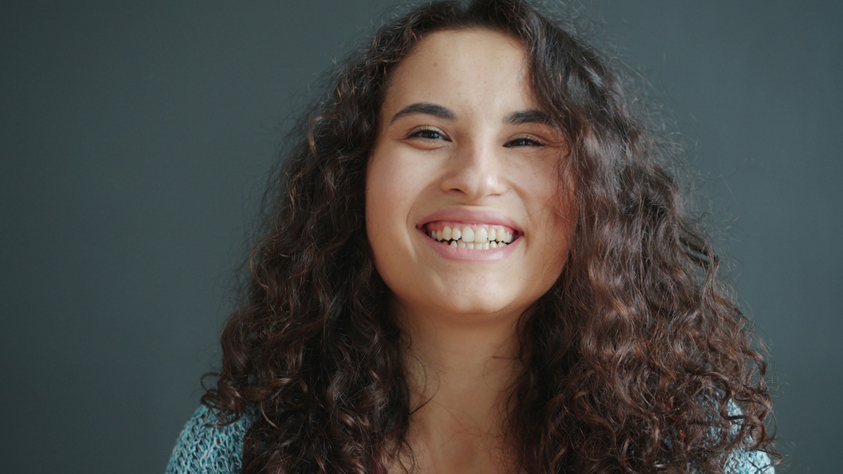 A young woman with curly hair smiling brightly, representing improved confidence and wellbeing.