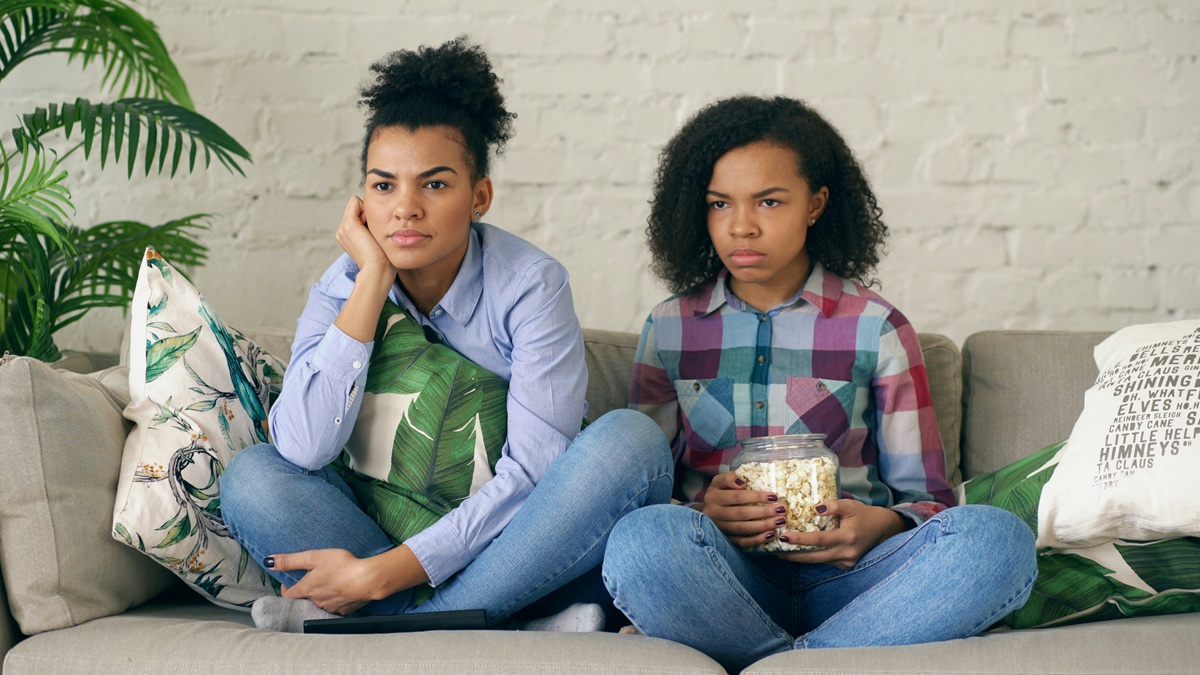 Two young women sitting on a sofa looking worried and pensive.